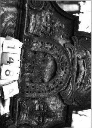 Grabstein 148 (Index: 99751968) Material: Sandstein Zustand: stark verwittert mit Textverlust Maße HxBxT: 142x99x10 cm Beschreibung: Stele, in Voluten auslaufend. Rundbogenaufsatz, Schriftfeld in Wappenschildform Symbolik: drei Kronen: Grabstein 148A