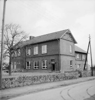 Volksschule: Dorfstraße: Erweiterungsbau: links Schulhof mit Baum: davor Mauer mit Zaun: im Vordergrund Dorfstraße