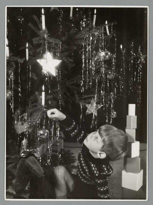 Tomas, der Sohn der Gremmlers, mit Spielzeug vor einem Weihnachtsbaum