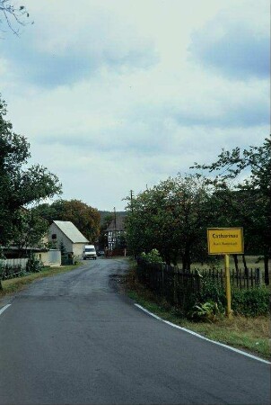 Straße mit Ortsschild, umzäunter Obstgarten