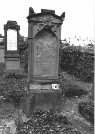 Grabstein 36 (Index: 99808466) Material: Sandstein Zustand: stark verwittert, beschädigt, mit Textverlust Maße HxBxT: 195x62x32 cm Beschreibung: Stele, getreppter Sockel, giebelartiger Abschluß mit Verdachung und Eckakroteren, Schriftfeld eingetieft mit Rundbogenabschluß Symbolik: gestelztes Fries: Grabstein 36