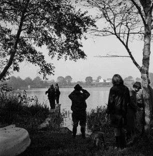 Jagdhundeprüfung: vorn rechts Teilnehmer mit ihren Hunden: in der Mitte Mann mit Fernglas: hinten links Teilnehmer auf Steg: hinten Poggensee
