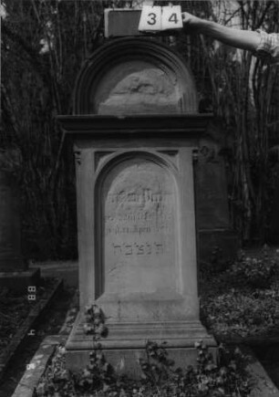 Grabstein 34 (Index: 99792843) Material: Sandstein Zustand: stark verwittert mit Textverlust Maße HxBxT: 156x65x36 cm Beschreibung: Stele, Sockel profiliert, eingezogener Rundbogenabschluß mit Verdachung, Schriftfeld eingetieft mit Rundbogenabschluß: Grabstein 34