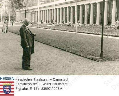 Stock, Christian (1884-1967) / Porträt, vor Brunnenkolonnaden in Wiesbaden stehend, Ganzfigur