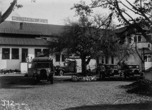 Expeditionsfahrzeuge vor einem Hotel : Die Fahrzeuge der Expeditions vor dem Messina Hotel geparkt. Einige Expeditionsteilnehmer an den Fahrzeugen, weitere Personen vor dem Hotel.