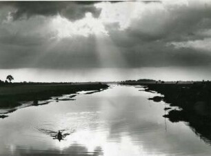 Impression. Die Sonne bricht durch die Wolken und spiegelt sich in der Süderelbe. Ein Ruderboot befindet sich auf dem Gewässer