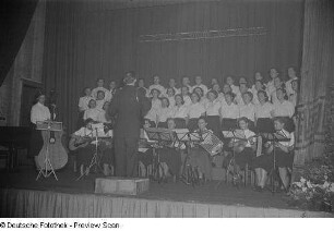 Chor, Chorleiter und Instrumentenensemble während eines Auftritts beim Bezirksausscheid der Volkskunstgruppen 1954