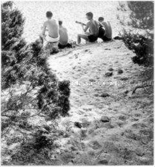 Blick auf vier Männer, die im Sand sitzen, einer spielt Gitarre