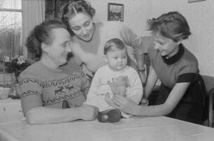 Drei Frauen und ein mit einem Teddybären spielendes Kleinkind