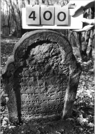 Grabstein 400 (Index: 99752652) Material: Sandstein Zustand: stark abgeblätt/verwitt. mit Textverlust Maße HxBxT: 93x56x7 cm Beschreibung: Stele, geschwungen eingezog. Rundbogenabschl. , Schriftfeld eingetieft: Grabstein 400