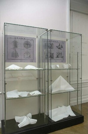 Serviettenfaltkunst. Dresden-Pillnitz, Kunstgewerbemuseum. 2007.06.30-10.31. Zwei Standvitrinen mit gefalteten Tischservietten (X. und XI. Figur) von J. Sallas