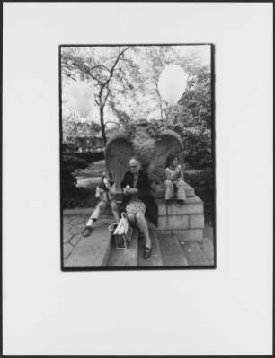 Frau mit zwei Kindern mit Luftballons an einer Adlerskulptur