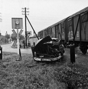 Siebenbäumen (Kreis Herzogtum Lauenburg): Bahnstrecke zwischen Bad Oldesloe und Ratzeburg: Bahnübergang der Landstraße zwischen Bad Oldesloe und Ratzeburg: Filmaufnahmen der Reginald Puhl Filmproduktion aus Hamburg-Wandsbek zum Dokumentarfilm "Todesfallen": nachgestellter Bahnunfall einer Dampflokomotive mit einem Pkw: in der Mitte beschädigter Pkw: dahinter Bahnübergang: rechts Güterwaggons: links Signalanlagen, Wartehäuschen und Strommast: dahinter Straße mit parkenden Pkws, Fußgängern und Bäumen