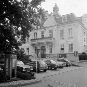 Rathaus: Paul-von-Schoenaich-Straße: Außenaufnahme: vorne Bergstraße, Parkplatz mit Autos, Verkehrsschilder, links Baum: vorne links Fleckenspumpe [Handpumpe zur Wasserversorgung] mit Schild "1842"