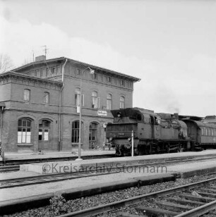 Bahnhof: davor Kinder mit Fahrrädern: vorn Gleisanlagen und Bahnsteige mit haltendem Personenzug
