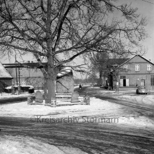 Lasbek-Dorf: Ehrenmal mit Friedenseiche: Dorfplatz mit Straßen: hinten Mopedfahrer: im Hintergrund Bauernhäuser: rechts davor VW-Käfer: Winter
