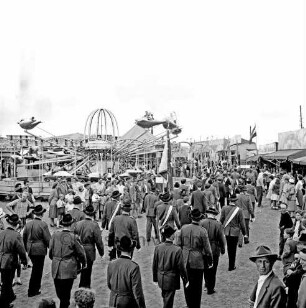 Schützenfest: Veranstalter Bürgerschützengilde von 1627 e.V. Bad Oldesloe: Umzug: Einmarsch auf Festplatz an Sehmsdorfer Straße: Schützenvereine marschieren mit Fahnen [Rückenansicht]: zu beiden Seiten Zuschauer mit Kindern: hinten Raketen-Karussell in Fahrt, Jahrmarktstände, 28. Juni 1959