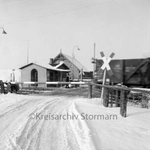Bahnübergang bei Schrankenposten 60 mit vorbeifahrendem Güterzug: Bahnstrecke zwischen Hamburg und Lübeck: rechts Andreaskreuz: hinten links Bahnwärterhaus: Winter
