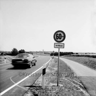 Kreisstraße Richtung Barkhorst: vorn Straßenschild: links fahrender Pkw: rechts Radweg: im Hintergrund Barkhorst mit Silo