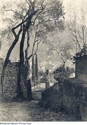 Gasse zwischen zwei Mauern. Blick zu einem Eingangstor oberhalb einer Stadt (wahrscheinlich in Italien)