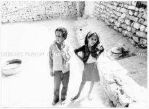 Ein Junge und ein Mädchen, beide barfuß, im Hintergrund Steinmauern