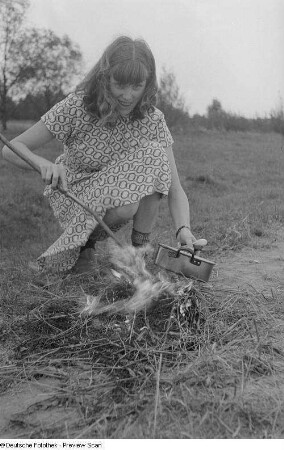 Renate Rössing setzt einen Kochtopf auf ein Feuer im Freien