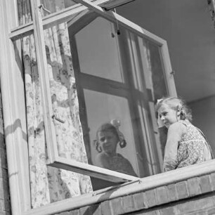 Mädchen mit Zöpfen und Schleifen schaut aus dem Fenster