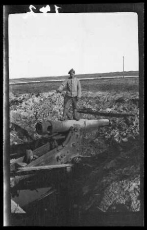 bei Kowno (=Kaunas, Litauen): Lafette mit großer Kanone in einer Geröllsenke, darauf ein Soldat mit Feldmütze stehend ("Geschütz bei Kowno")