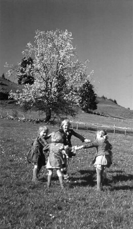 Kinder beim Ringelreihen auf einer Wiese, wahrscheinlich im Allgäu