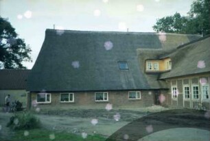 Papierholz 1: Gaststätte Zur Hahnheide: giebelständiges Bauernhaus mit Reetdach: Teilansicht: links Traufseite Altbau mit Tür: rechts neuer Querbau bei Fertigstellung, rückwärtige Traufseite [angeschnitten]