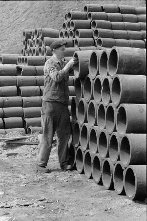 Lagerung von Rohren (Inneres ist mit Schlacke als Verschleiß- und Dämmmaterial ausgekleidet). Arbeiter rückt ein Rohr auf dem Stapel
