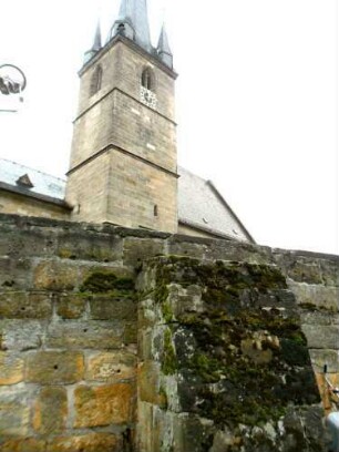 Ansicht von Nordosten mit Kirchturm (im Kern frühgotisch) über Kirchhofmauer mit erhaltenen Zangenlöchern der Hebezeuge in den Werksteinen