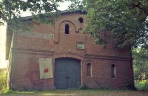 Am Markt (10): traufständiges Backsteingebäude mit umlaufendem Gesims: Giebelseite Wirtschaftstrakt mit Scheunentor, an Fassade verblichene Aufschrift "Fritz Meins"