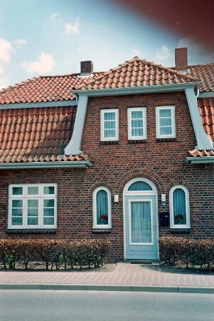 Lübecker Straße 14: traufständiges Wohnhaus aus Backstein mit Krüppelmansarddach: Straßenfront, Teilansicht: Eingangstür mit halbrundem Oberlicht, beiderseits Rundbogenfenster, Sprossenfenster, mittig Zwerchgiebel mit Sprossenfenstern: Vorgartenhecke