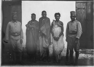 Kolonialsoldaten und Gefangene : Gruppenportrait von zwei deutschen Kolonialsoldaten und drei Gefangenen in Ketten