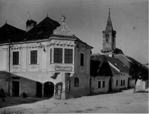 Rust/ Burgenland. Österreich. Ansicht eines zweigeschossige Bürgerhauses auf dem Hauptplatz des Ortes - auch "Haus zum Auge Gottes". Im Hintergrund die Katholische Pfarrkirche