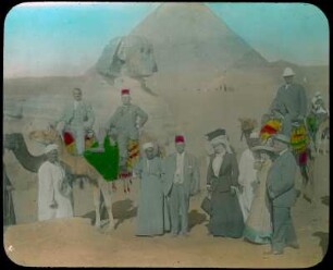 Gizeh (Ägypten). Touristen und einheimische Führer mit Kamelen vor der Sphinx und den Pyramiden von Gizeh