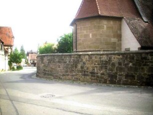 Ansicht von Nordosten mit Chor (im Kern Gotisch) über Kirchhofmauer mit Werksteinen im Mauersteinverband und erhaltenen Zangenlöchern (Wehrgang mit Steinbrüstung im 18 Jh abgetragen)