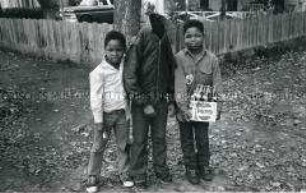 Porträt von drei kleinen dunkelhäutigen Jungen, der mittlere versteckt seinen Kopf in der Jacke