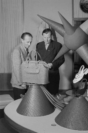 Zwei Männer begutachten eine Tasche und Schuhe des VEB Vogtländische Wachstuchfabrik Treuen in Specks Hof auf der Leipziger Herbstmesse 1955