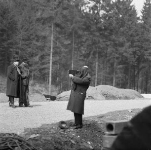 Ein Mann fotografiert mit einer Mittelformatkamera, zwei Männer beobachten ihn dabei