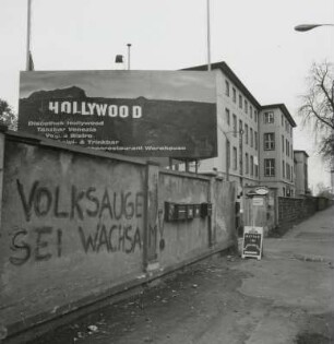 Mauer mit Inschrift "Volksauge sei wachsam!" und Reklameschild für Diskothek "Hollywood