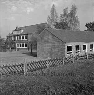 Volksschule: Schultwiete: vorn Rasen mit Jägerzaun: rechts Erweiterungbau: dahinter altes Schulgebäude: hinten Bäume