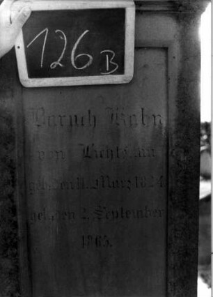 Grabstein 126 (Index: 100111259) Material: Sandstein Zustand: beschädigt und leicht verwittert Maße HxBxT: 205x57x48 cm Beschreibung: Stele, getreppter Sockel, Abdeckplatte mit Volutenaufsatz, rechteckige Schriftfelder eingetieft Symbolik: Blüten, Voluten: Grabstein 126B
