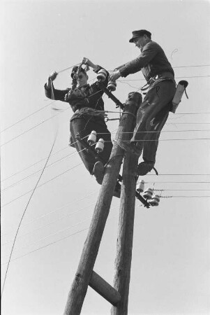 Energieversorgung. Arbeiten an einer Oberleitung. Ansicht mit zwei Arbeitern, auf einem Mast arbeitend