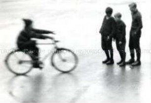 Drei Jungen schauen einem Radfahrer zu