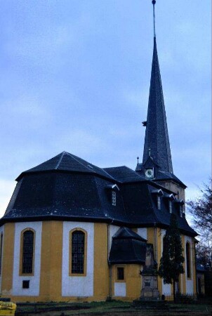 barocke Kirche mit hohem spitzem Turmhelm; davor Kriegerdenkmal