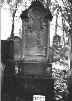 Grabstein 1052 (Index: 99899669) Material: Sandstein Zustand: fast völlig verwittert Maße HxBxT: 177x58x27 cm Beschreibung: aufgesockelte Stele mit eingezogenem Rundbogenabschluss, Akanthusaufsätze auf Einzügen und Giebel, Schriftfeld mit Maßwerkbögen Symbolik: Akanthus: Grabstein 1052