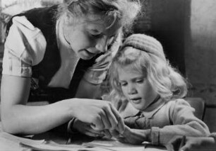 In einem Kindertagesheim. Eine Erzieherin erklärt einem Mädchen etwas. Aufgenommen 1951