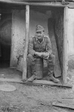Zweiter Weltkrieg. Zur Einquartierung. Sowjetunion. Angehöriger der deutschen Wehrmacht, vor einer Bauernhütte sitzend
